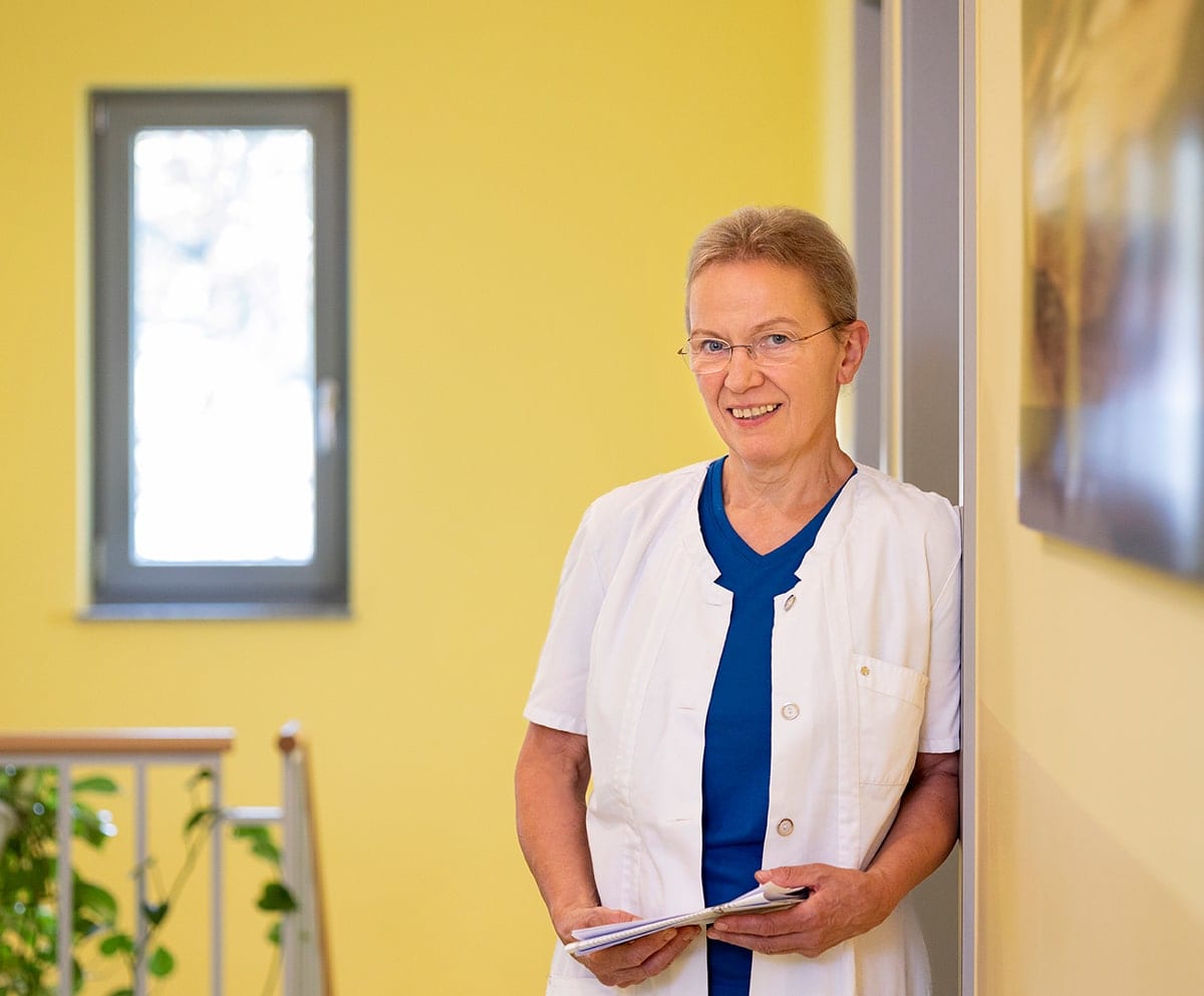 Frau mit weißem Kittel, an einer Wand angelehnt