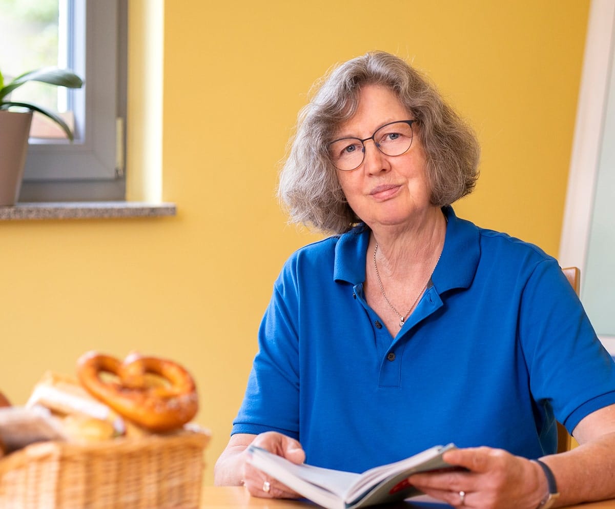 Frau mit blauem Shirt mit Buch in der Hand an einem Tisch sitzend